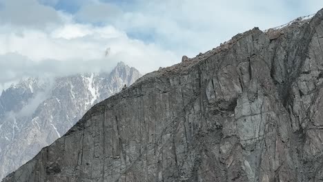 Aerial-Dolly-Left-Across-Mountain-Wall-To-Reveal-Passu-Cones-In-the-Karakoram-Range-Hiding-In-Clouds