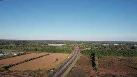 Aerial-drone-forward-moving-shot-over-two-way-roads-along-rural-landscape-with-aututmn-blue-skies-at-daytime