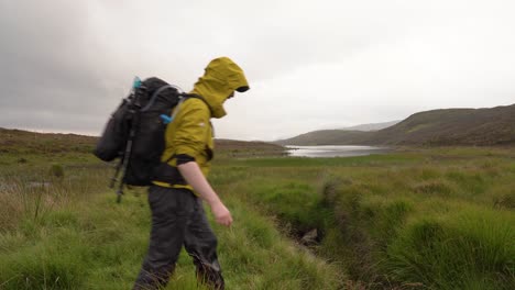 Hiking-in-Yellow-Jacket-Jumping-over-Stream-in-Scottish-Landscape
