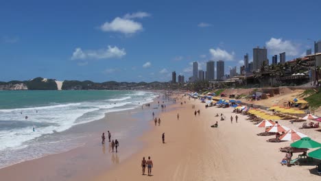 Flying-low-over-people-on-Sand-beach-and-Skyline-of-Ponta-preta