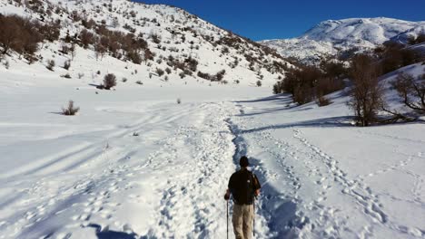 Man-in-khaki-colored-hiking-pants-and-black-polo-does-Nordic-walking-in-his-mountain-boots-in-a-thick-layer-of-snow-in-Mount-Hermon-in-Israel-on-a-sunny-day