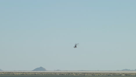 A-helicopter-looking-small-in-the-distance-flying-over-the-dusty-Dakar-Rally-desert