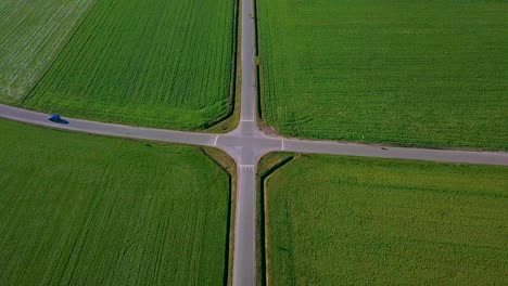 Aerial-view-of-a-perfect-symmetrical-crossroad-with-green-fields-with-1-blue-car