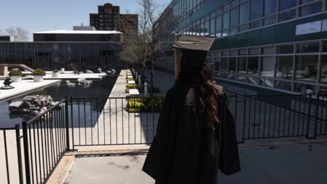 Female-college-graduate-wearing-cap-and-gown-walking-outside-with-video-from-behind-in-slow-motion