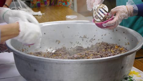 Purple-rice-and-pork-meat-mixture-being-spooned-from-large-bowl-into-small-pink-bowls-for-weight-measurement-in-busy-kitchen-area