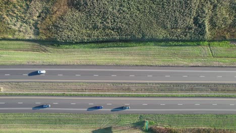 Aerial-drone-top-down-shot-over-two-way-highway-passing-through-rural-green-landscape-at-daytime