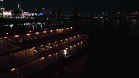 Aerial-view-around-a-steamboat-driving-on-the-Ohio-river,-night-in-Cincinnati,-USA---circling,-drone-shot