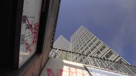 Tilt-up-reveal-shot-of-a-tall-modern-skyscraper-office-building-with-graffiti-and-vandalism-in-the-foreground,-a-bright-clear-blue-sky-in-the-background
