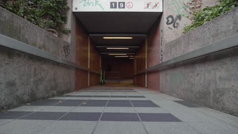 Low-dolly-forward-shot-entering-a-subway-station-tunnel-with-graffiti-on-the-walls,-and-electric-scooters-ready-to-use