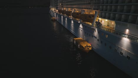 Aerial-drone-rotating-shot-over-tender-boats-unloading-and-loading-passengers-on-a-cruise-ship-at-night-time