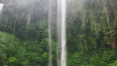 Antenne-Des-Wasserfalls-In-Einem-Grünen-Dschungel-Mit-Sprühnebel,-Der-Das-Kameraobjektiv-Abdeckt-Und-Reflexionen-Verursacht