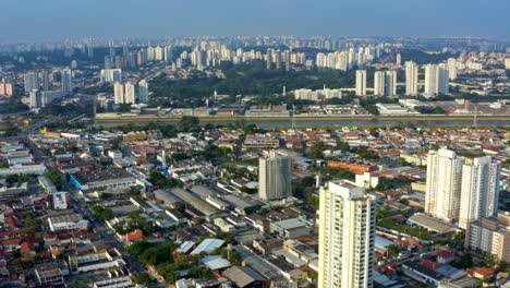 Aerial-drone-tilting-up-dolly-in-shot-of-the-south-part-of-São-Paulo,-Brazil-from-the-Socorro-neighborhood-near-the-Guarapiranga-Reservoir-with-skyscrapers,-roads,-rivers,-and-houses-on-a-fall-evening