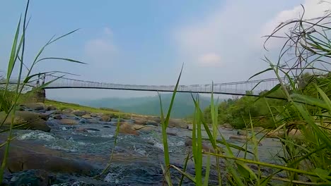Isolierte-Eiserne-Hängebrücke-über-Fließendem-Fluss-Mit-Berg--Und-Blauem-Himmelshintergrund-Am-Morgenvideo-Wird-In-Nongjrong-Meghalaya-Indien-Aufgenommen