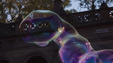 Big-Giant-Soap-Bubble-Shape-Floating-in-Air,-Dragged-by-Breeze,-Moving-Expanding-and-Bursting,-Colorful-Transparent-Shape-Blast-Burst-Outside-in-Park