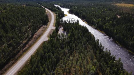 Aerial-view-following-river-and-road-in-large-coniferous-forest-in-Finland