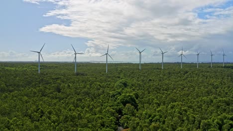 Spinning-wind-turbines-against-blue-sky-in-lush-forested-onshore-area