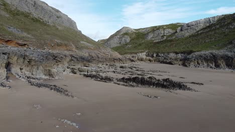Aerial-Drone-Shot-Retreating-Along-Beach-from-Valley-Entrance-Showing-Sea-Caves-and-Golden-Sand-on-Mewslade-Bay-Waes-UK-4K