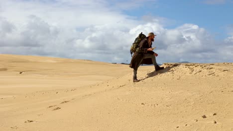 A-trekker-wearing-a-pack-looks-at-the-sand-patterns-in-epic-sand-dunes