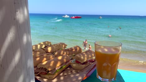 Delicious-sandwiches-at-a-beautiful-beach-bar-with-fresh-orange-juice,-enjoying-summer-with-dreamy-holiday-sea-view-in-Ibiza-Spain,-vacation-destination,-4K-shot