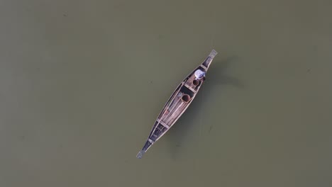 Local-Asian-fisherman-fishing-in-dirty-river-water-in-small-wooden-boat,-top-down