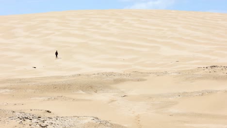 A-young-boy-walks-off-into-the-distance-of-a-big-sand-dune-in-Australia