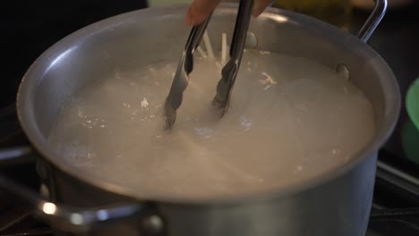Closeup-shot-of-boiling-noodles-in-an-aluminium-kitchen-cooking-utensil-using-a-tong