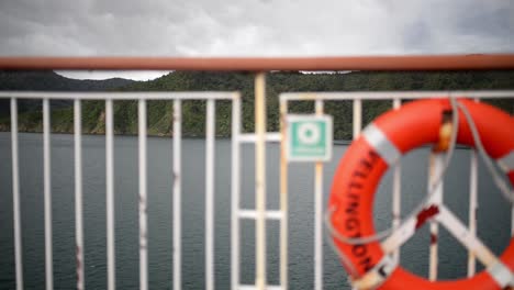 Life-buoy-out-of-focus-on-side-railing-of-a-large-ship-sailing-through-lush-fiords-in-New-Zealand