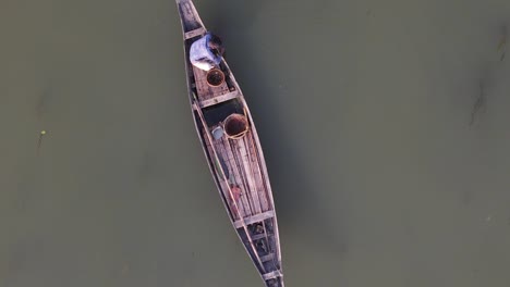 Asian-fisherman-fishing-in-traditional-wooden-boat,-aerial-top-down-view