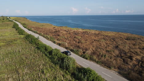 Car-Driving-Through-The-Empty-Road-Overlooking-The-Blue-Sea-In-Sumba-Island,-Indonesia