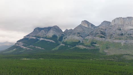 Aerial-dolly-in-over-green-forest-valley,-Canadian-Rockies-mountain-range-in-background-at-Banff-National-Park,-Alberta,-Canada
