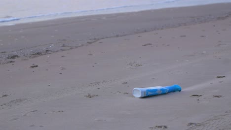 Blue-plastic-bottle-on-the-beach,-trash-and-waste-litter-on-an-empty-Baltic-sea-white-sand-beach,-environmental-pollution-problem,-calm-evening,-medium-shot