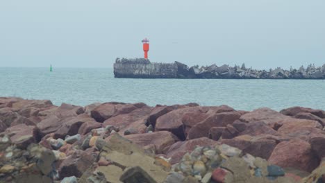 Distant-low-angle-view-of-stone-pier-near-the-Port-of-Liepaja-,-overcast-autumn-day,-red-port-navigation-beacon,-calm-sea