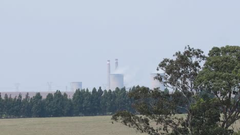 A-distant-shot-of-a-coal-fired-power-station,-as-thick-pollution-and-water-vapour-bellows-out-from-the-cooling-towers-as-the-plant-generates-electricity,-South-Africa