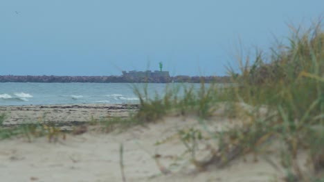 Distant-low-angle-view-of-stone-pier-near-the-Port-of-Liepaja-,-overcast-autumn-day,-white-sand-beach-in-foreground,-calm-sea