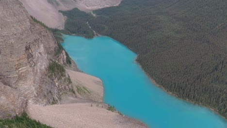 Aerial-lowering-over-emerald-Lake-Moraine-between-mountains-and-pine-tree-forest-at-Banff-National-Park,-Alberta,-Canada