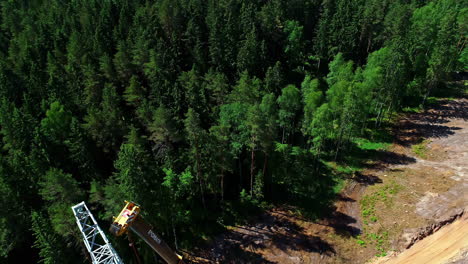 The-drone-above-and-revealing-high-voltage-electric-tower-with-engineers-working-and-an-attached-crane-in-the-middle-of-the-forest