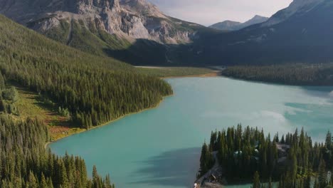 Aerial-rising-over-emerald-Lake-Louise-between-pine-woods-and-Canadian-Rockies-at-Banff-National-Park,-Alberta,-Canada