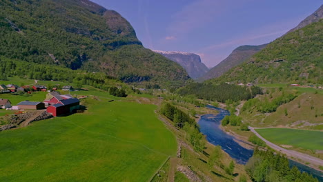Aerial-drone-forward-moving-shot-over-village-houses-on-lush-valley-in-mountainous-landscape-with-river-flowing-through-in-Aurland,-Norway-at-daytime