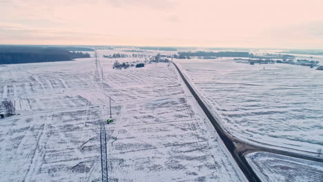 Industrial-worker-repairing-transmission-tower-during-snowy-winter-day-in-the-morning---aerial-backwards-flight