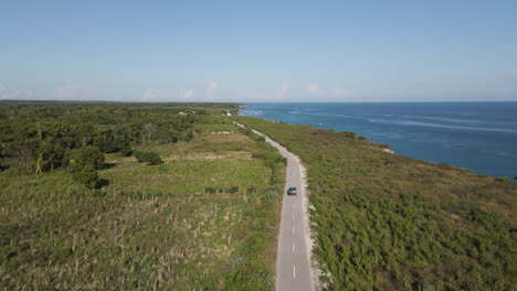 Car-Driving-On-The-Road-Overlooking-The-Blue-Sea-At-Daytime-In-Summer-In-Sumba-Island,-Indonesia