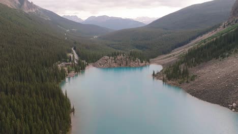 Aerial-dolly-in-of-turquoise-Lake-Moraine-surrounded-by-pine-tree-forest,-Canadian-Rockies-at-Banff-National-Park,-Alberta,-Canada