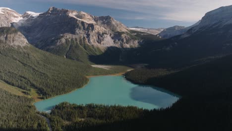 Aerial-dolly-out-of-emerald-Lake-Louise-surrounded-by-dense-pine-tree-forest-and-mountains-at-Banff-National-Park,-Alberta,-Canada