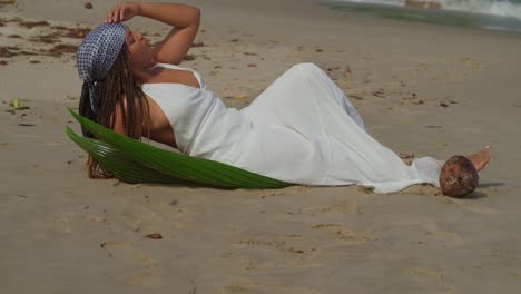Young-female-lays-in-the-golden-brown-sand-of-a-Caribbean-island-with-waves-crashing-in-the-background