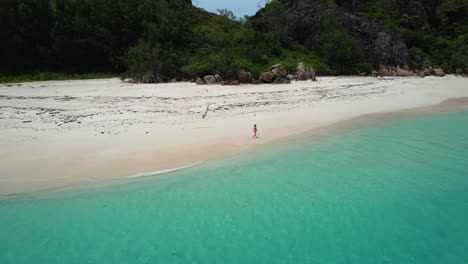 Aerial-view-of-Woman-walking-on-white-sand-beach-on-tropical-island-in-the-Seychelles