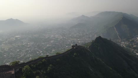 Alte-Filmische-Luftaufnahme-Der-Alten-Stadtfestung-Von-Jaipur-Mit-Atemberaubender-Szenischer-Nebliger-Landschaft-Stadtbild-In-Indien-Rajasthan