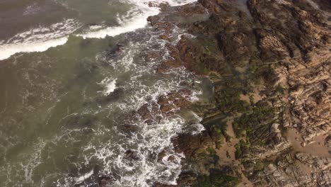 Hoher-Drohnenflug-über-Einen-Surfer,-Der-In-Die-Raue-See-Des-Atlantiks-In-Der-Nähe-Der-Felsigen-Küste-Von-Punta-Del-Este-In-Uruguay-Eindringt