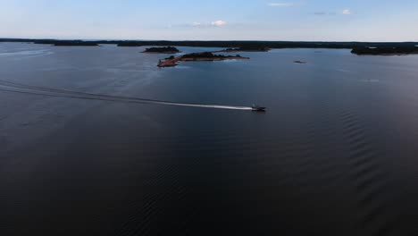 Aerial-view-of-a-speedboat-driving-in-the-Aland-archipelago,-summer-evening-in-Finland---pan,-drone-shot