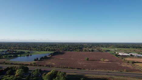 Beautiful-aerial-drone-forward-moving-shot-over-large-farmlands-beside-a-lake-on-an-autumnal-evening