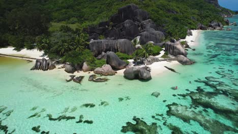 Pull-back-Aerial-of-boulders-kayaker-and-palm-trees-on-popular-Seychelles-Beach-on-La-digue-Island