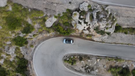 Straight-down-view-of-a-car-taking-a-u-turn-on-a-winding-mountain-road-in-Sa-Calobra,-Mallorca,-Spain